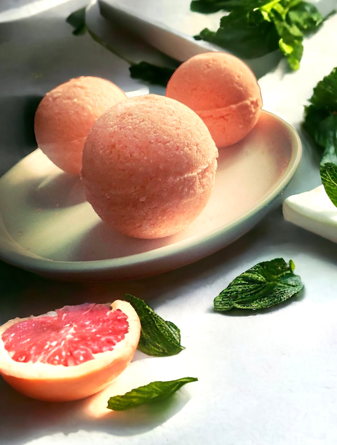 Three Nalim’s Aroma Grapefruit and Mint scented bath bombs on a plate surrounded by mint leaves and sliced grapefruit